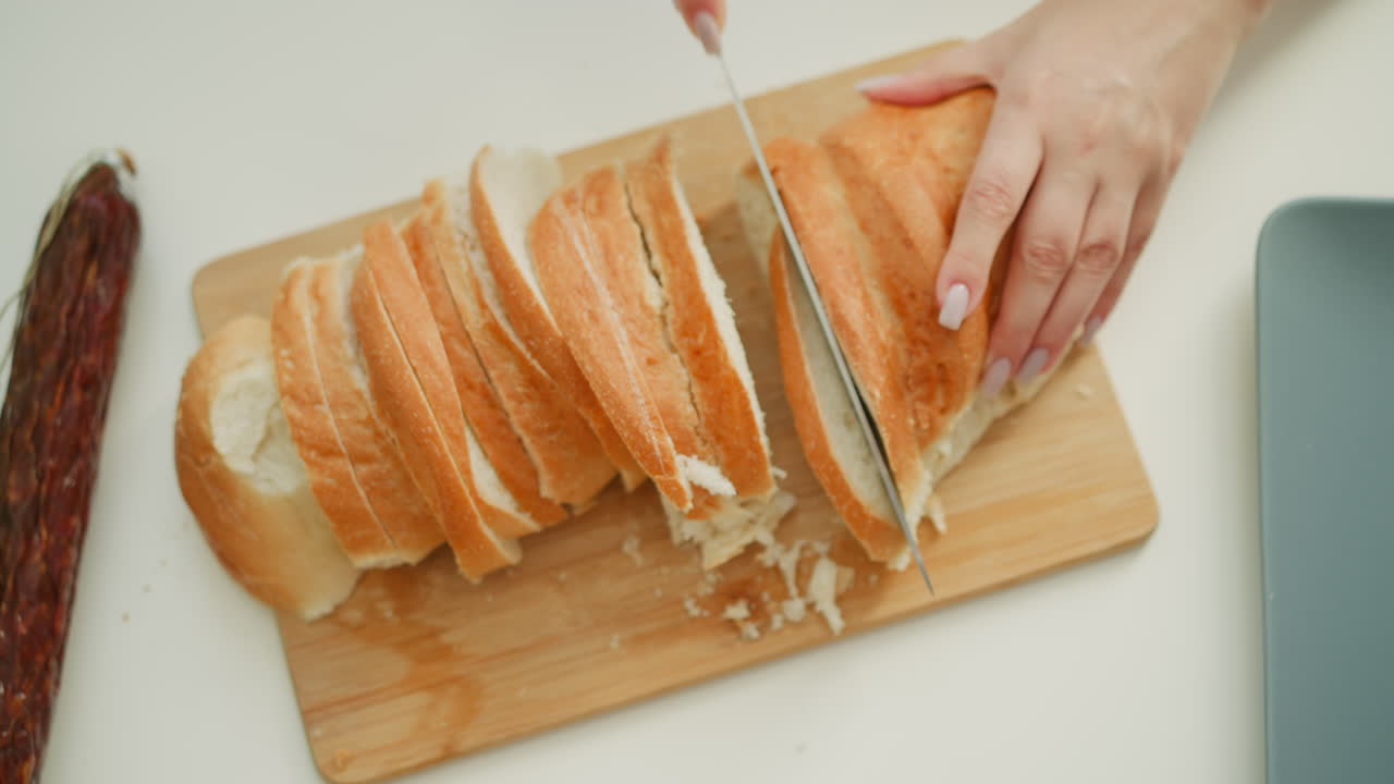 Close up of female baker hands holding firm baked cake and cutting with knife gently slicing into equal parts on neat white table under bright morning light, highlighting texture of crust