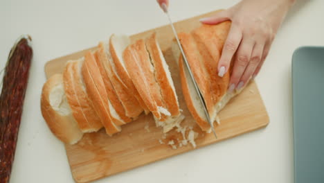 close up of female baker hands holding firm baked cake and cutting with knife gently slicing into equal parts on neat white table under bright morning light, highlighting texture of crust