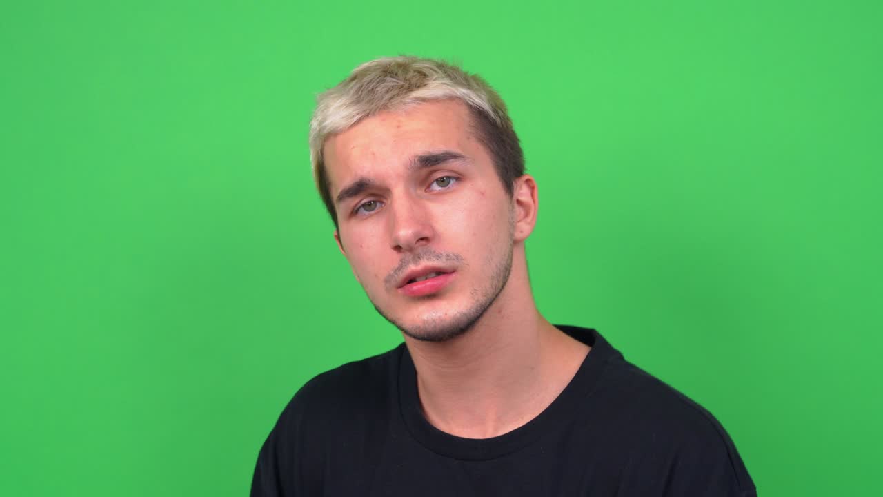 검은 티셔츠를 입고 은 머리카락을 가진 잘생긴 남자가 크로마키 클로즈업에서 카메라를 위해 포즈를 취하고, 십대 얼굴 피부를 가진 젊은 남자가 감각적으로 시를 송하거나 노래를 부른다.