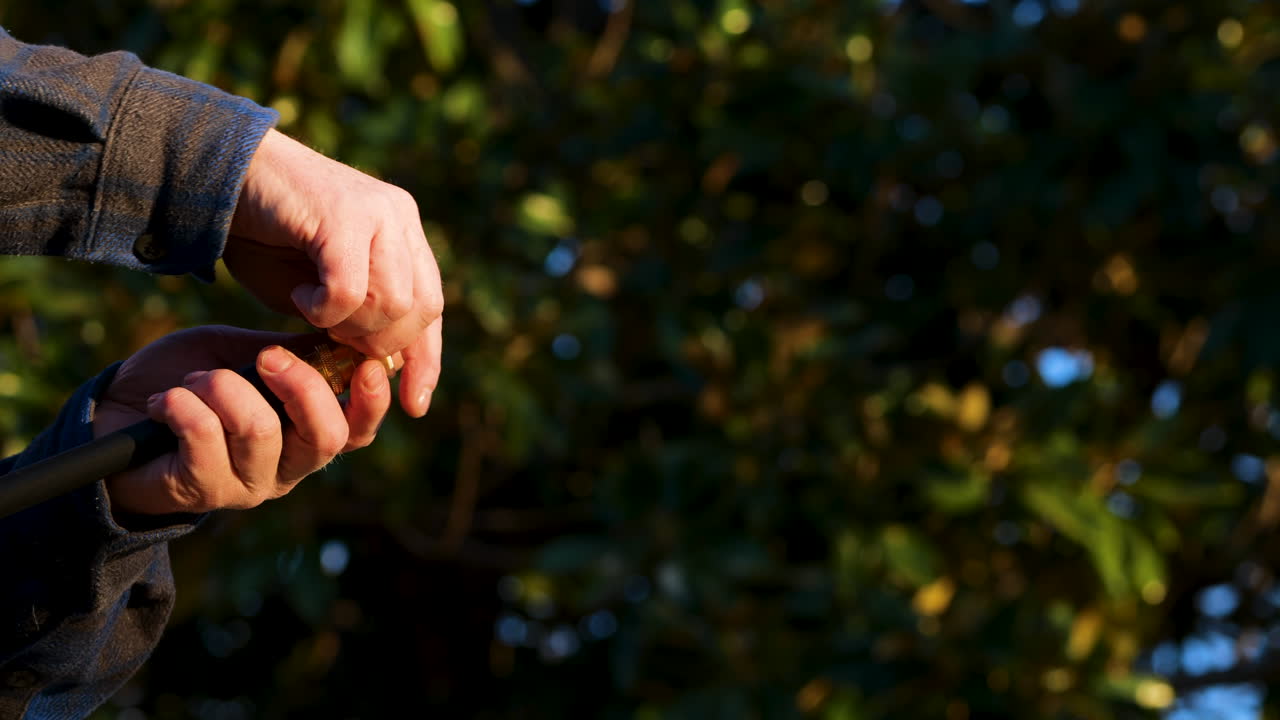 Male caucasian hands remove white nozzle from power washer with trees in the background