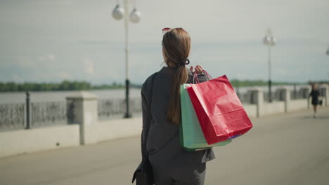 back view of lady walking with colorful shopping bags and black handbag, walking with people walking toward her in the blurred background, one person swinging her handbag from hand to hand