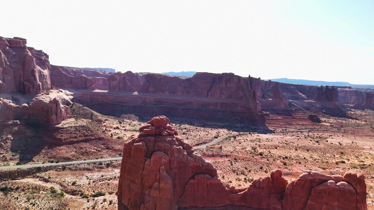 Splendido filmato stock del Parco Nazionale di Arches, USA, durante un pomeriggio luminoso. La luce solare brillante illumina le maestose strutture di arenaria rossa e il paesaggio desertico sotto un cielo azzurro limpido.