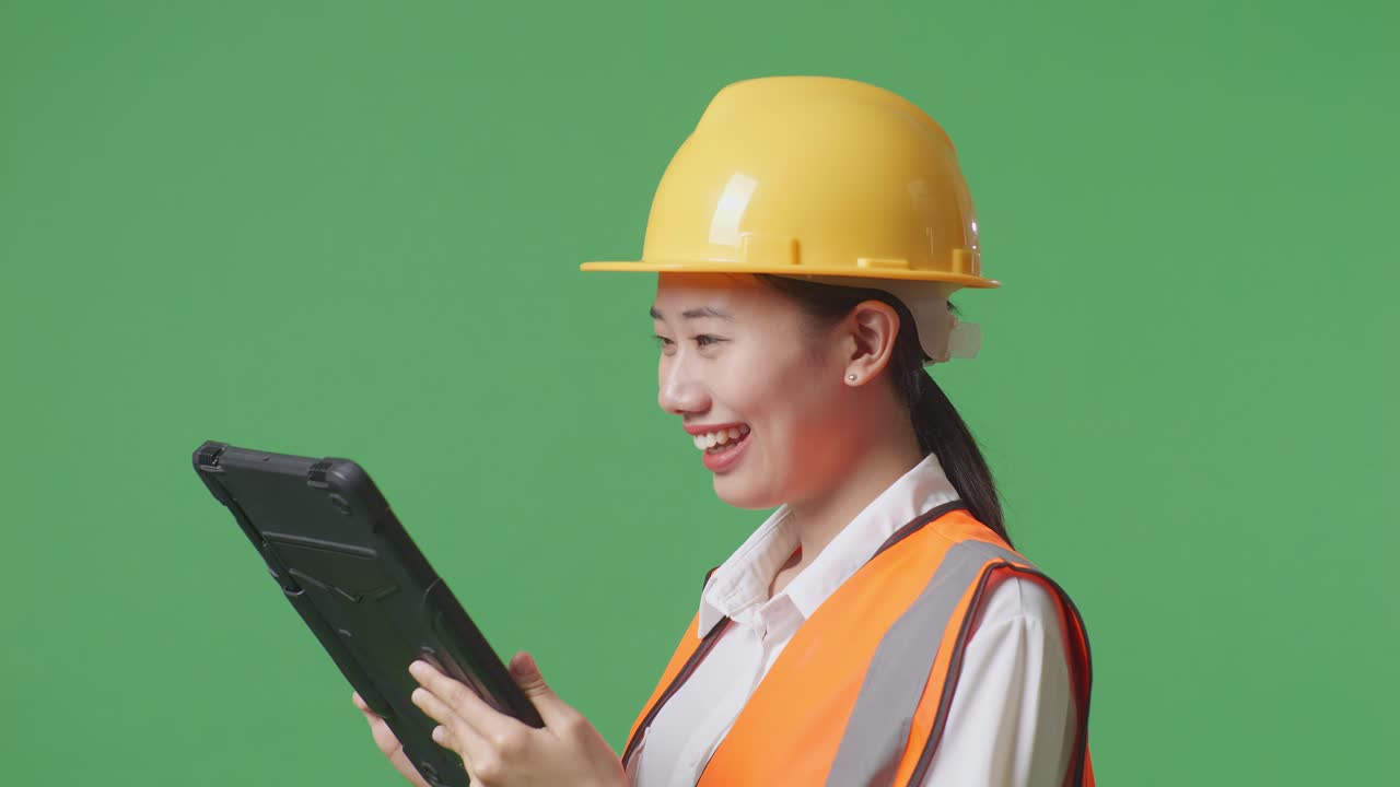 Close Up Side View Of Asian Female Engineer With Safety Helmet Working On A Tablet While Standing In The Green Screen Background Studio