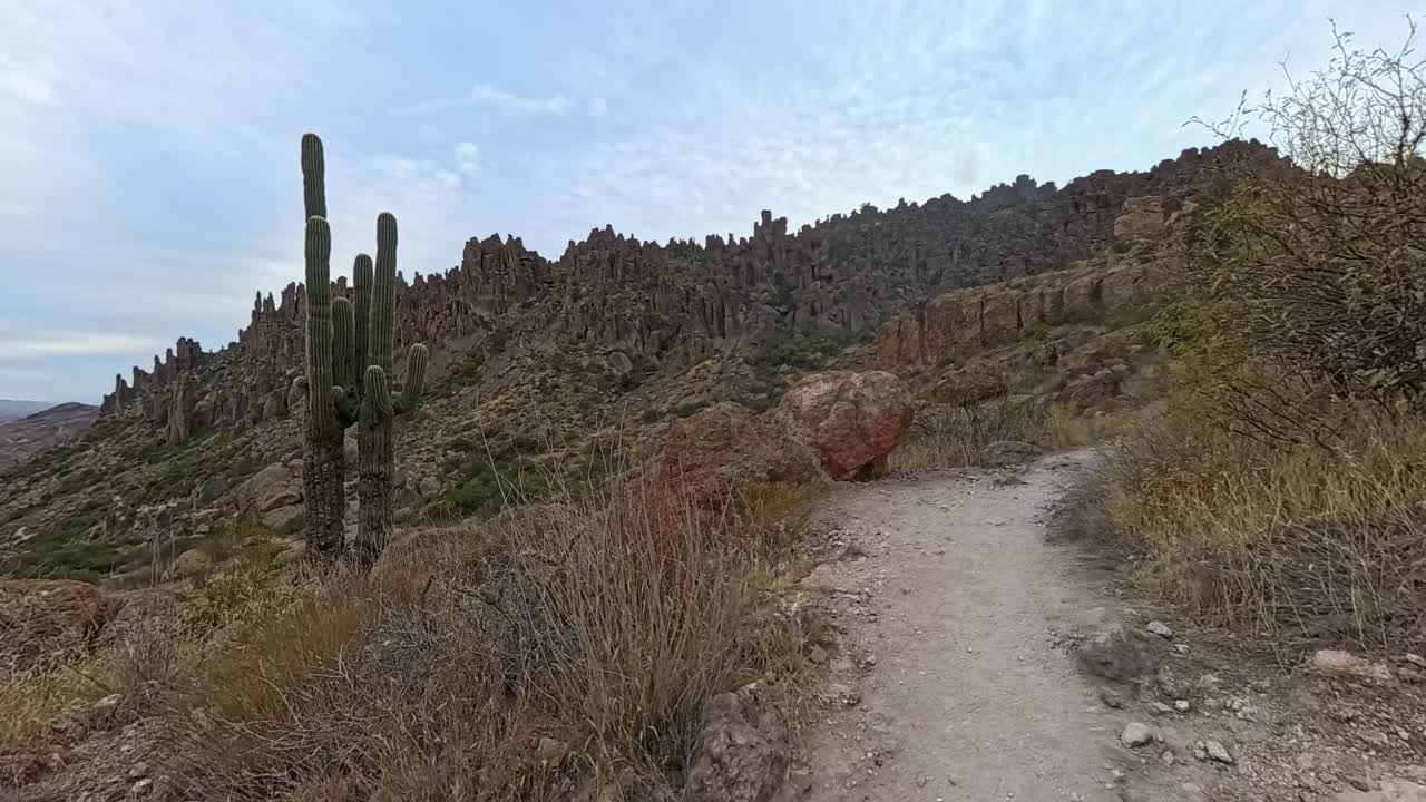 Time-lapse establishing shot of desert landscape in Arizona. Cactus and a hiking trail with a mountain view. Fast clouds moving during the day and sun shining and blue sky.
