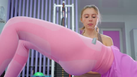 instructor de gimnasia entrenadores mujer realizando ejercicios de levantamiento de cintura en una alfombra de ejercicio, sesión de entrenamiento de fuerza en un gimnasio moderno con equipos de fitness, iluminación brillante y bolas de ejercicio en el fondo