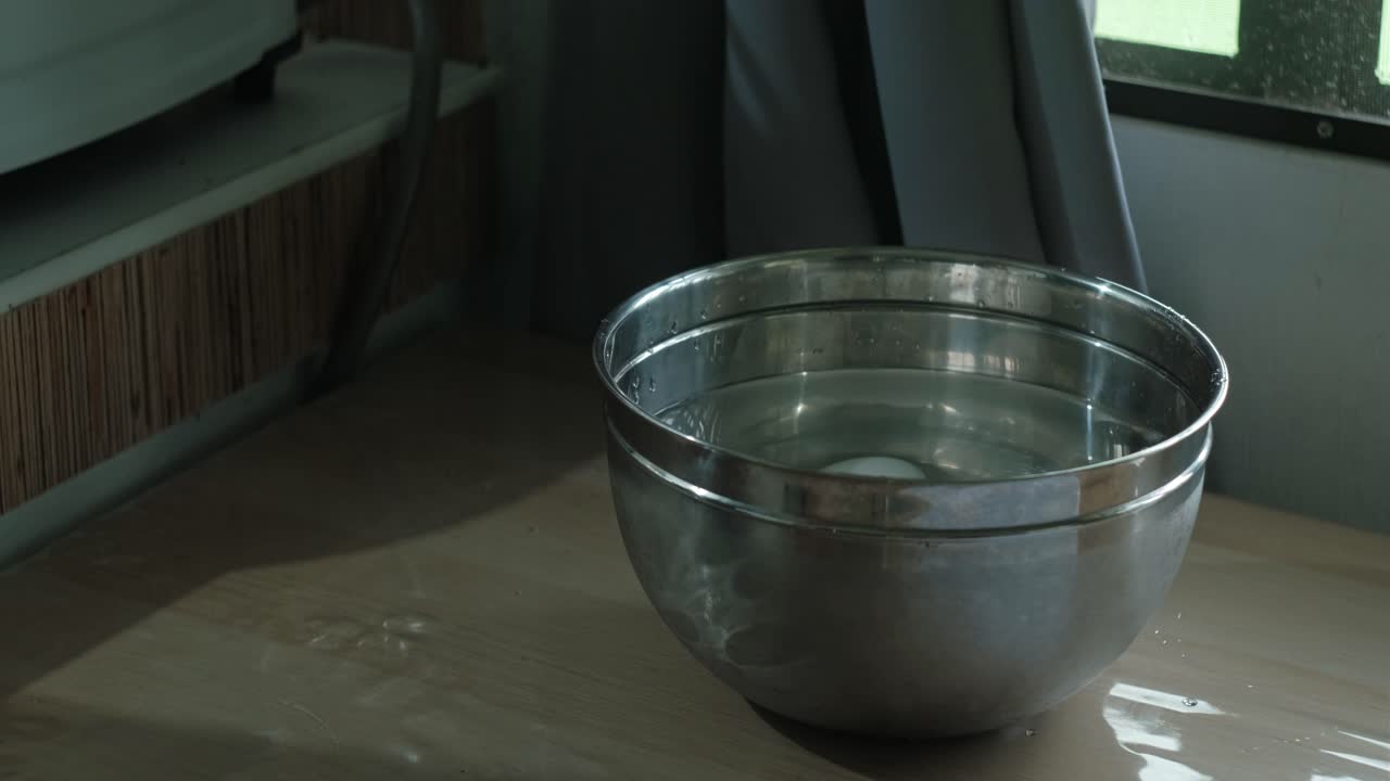 ein gekochtes ei in eine rostfreie schüssel mit wasser legen. nahaufnahme