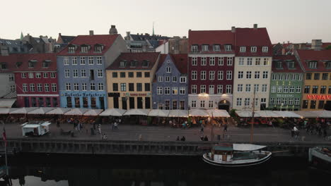 Puesta-De-Sol-Sobre-Nyhavn-En-Copenhague-Con-Un-Ambiente-Acogedor,-Gente-Y-Barcos-En-El-Canal