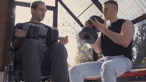 disabled man in wheelchair and his personal trainer working out with dumbbell at home