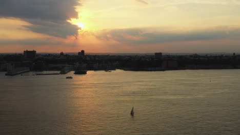 drone ascends, truck right up to golden sunset with ferry - sailboat on the hudson river with new jersey in the background