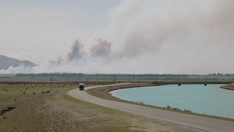 campista que se acerca conduciendo a lo largo de la carretera del canal con fuego salvaje activo y nubes de humo gigantescas en el fondo