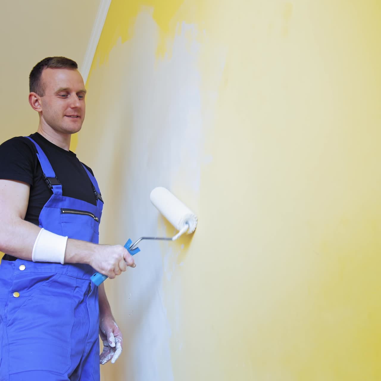 Man painting walls at home. Handsome man in work overalls paints the wall with a roller