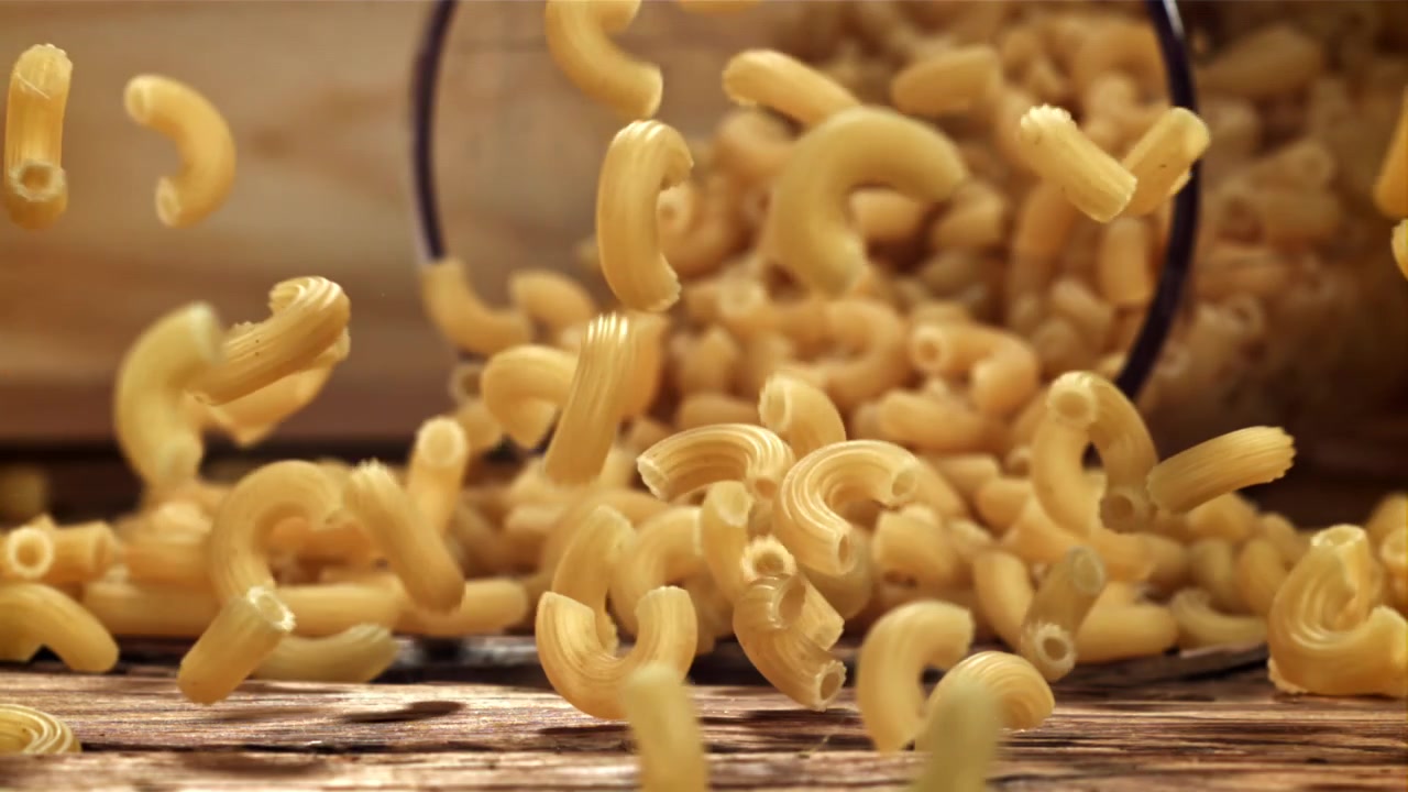 Maccheroni a gomito secchi che cadono al rallentatore su un tavolo di legno