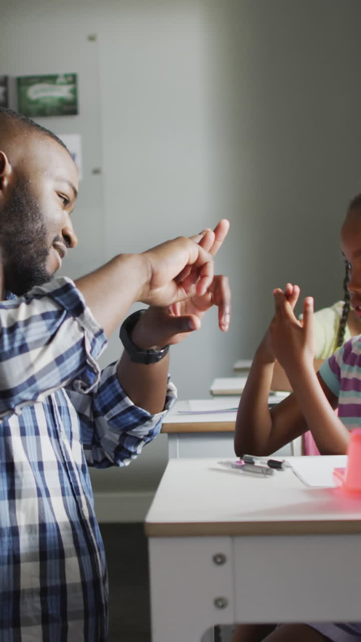 Video of happy african american teacher learning african american girl how to count in classroom