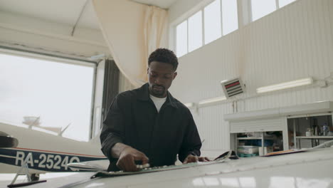 black male technician taking wrench to repair aircraft in aviation hangar