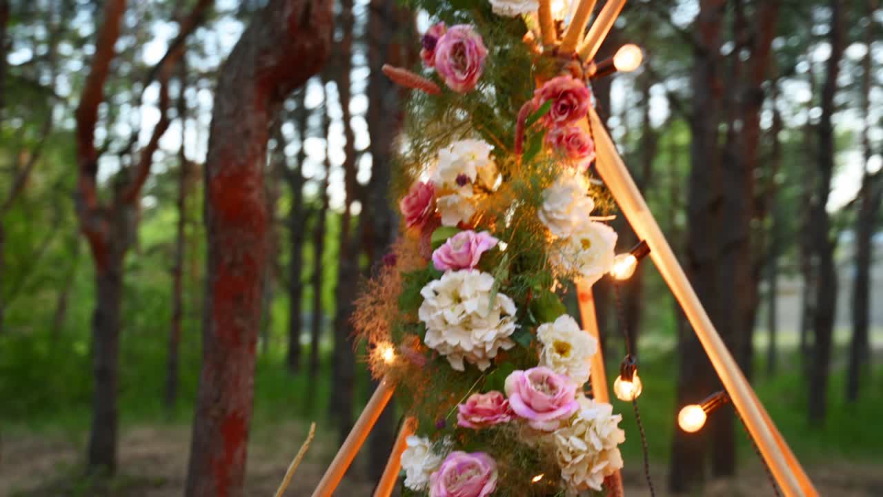 보헤미안 티피 나무 아치, 분홍색 장미, 카에 불, 파스 잔디, 야외에 요정 빛으로 포장, 밤에는 소나무 숲에서 결혼식 장소.