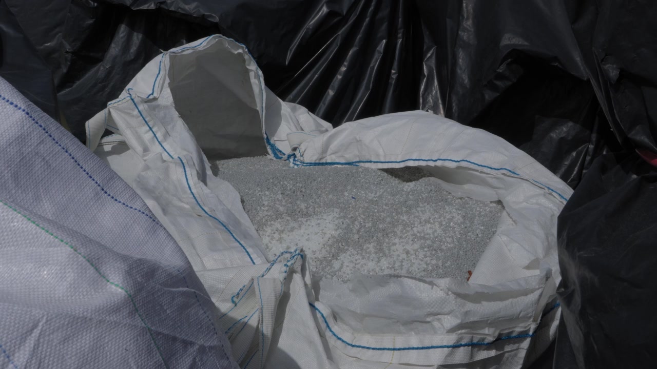 Ground Plastic Granules Filling Open White Woven Bulk Bag At Plastic Recycling Facility