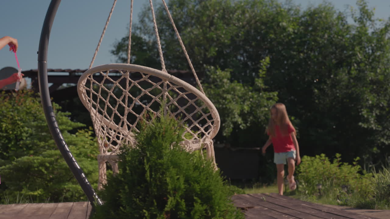 Children Playing Outdoors Happily Together, Lively Family Bonding With Playful Swings On Sunlit Porch, Happy Mother And Child Engage With Swinging On Bright Garden Deck Surrounded By Greenery