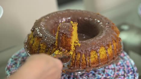 cortando un simple pastel de zanahoria casero con salsa de chocolate en un plato blanco con una espátula de metal levantando el caramelo con el plato