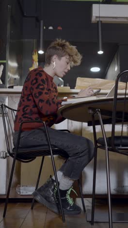 young woman focused on her phone and laptop at a cafe table