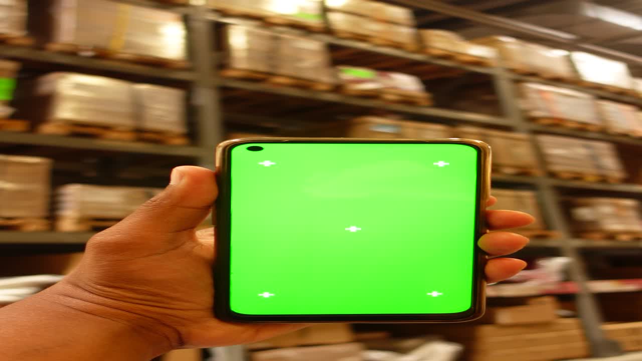 mano sosteniendo un teléfono inteligente de pantalla verde en un almacén