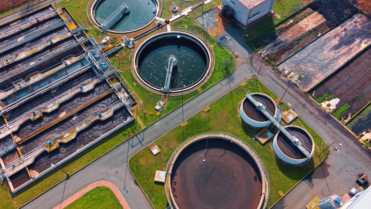 Aerial view of sewage treatment plant with circular clarifiers. Overhead shot of industrial water tanks and equipment on grass background
