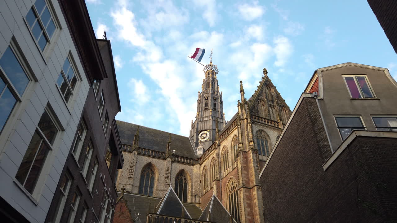 The Grote Kerk during King's Day with the Dutch flag waving on top of it during a sunny day in Haarlem