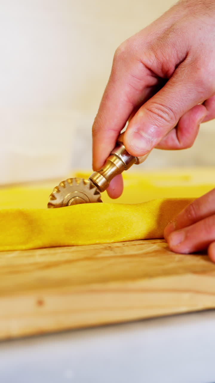 Primo piano verticale ravvicinato dello chef che taglia l'impasto della pasta fresca con una rotella dentellata su un tagliere di legno in una cucina professionale