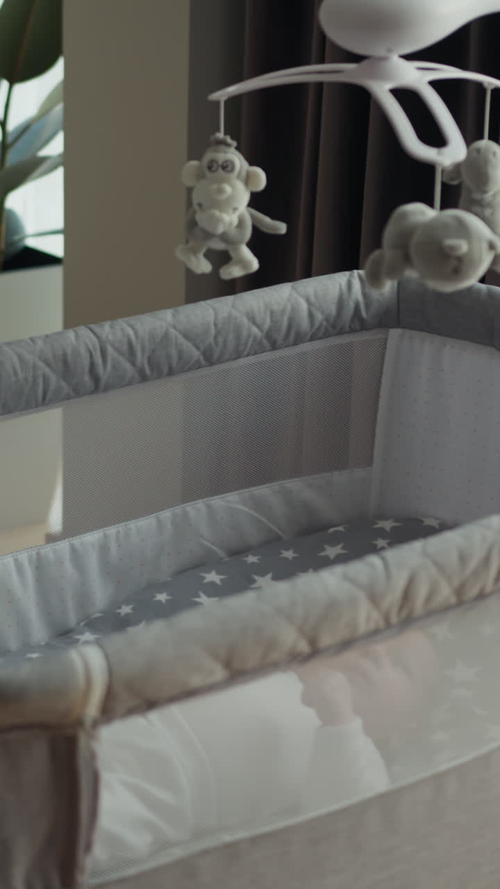 Un neonato riposa serenamente in una culla grigia con una giostrina con giocattoli di peluche sopra