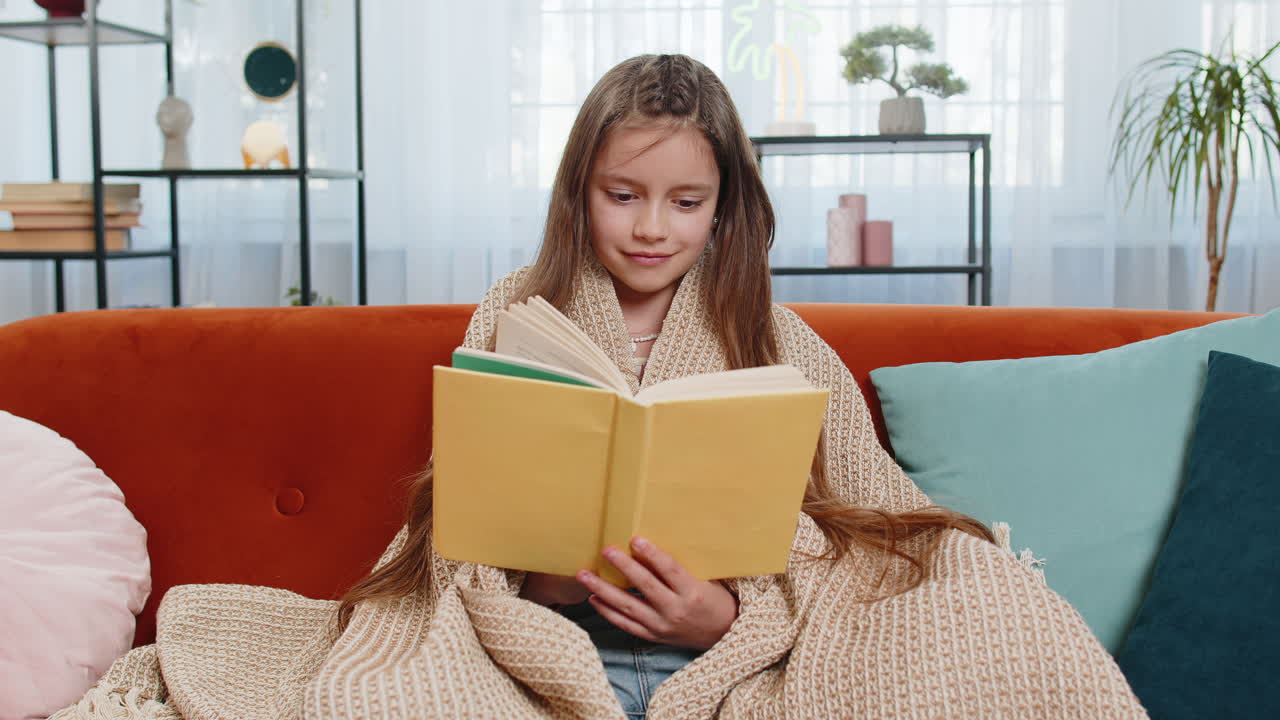 Bambino avvolto in una coperta rilassato che legge un libro che gira le pagine sorridendo che si gode dell'istruzione letteraria
