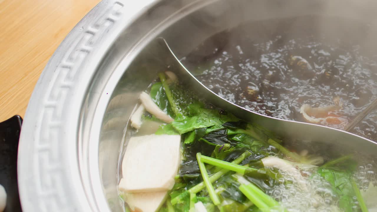 Chopsticks cook sliced meat in steaming dual broth hotpot with fresh vegetables, overhead view
