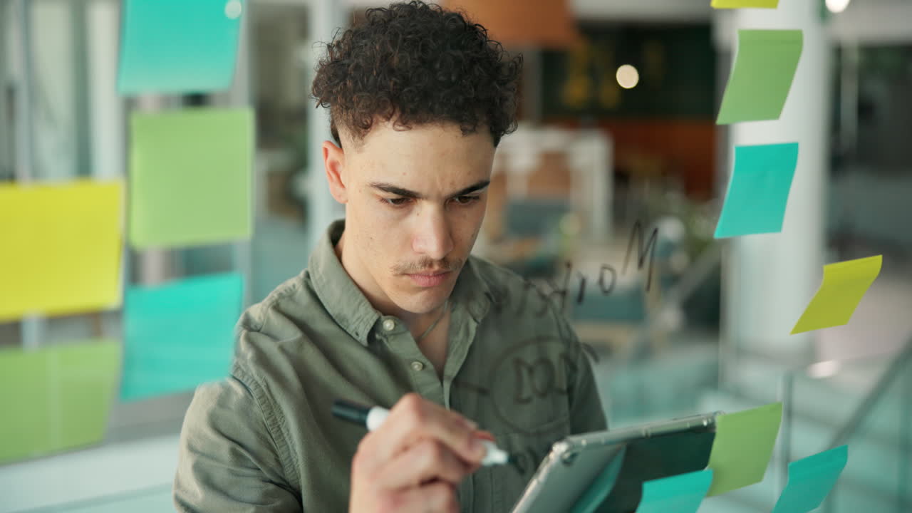 Young Man Brainstorming Ideas on Glass Board in Modern Office
