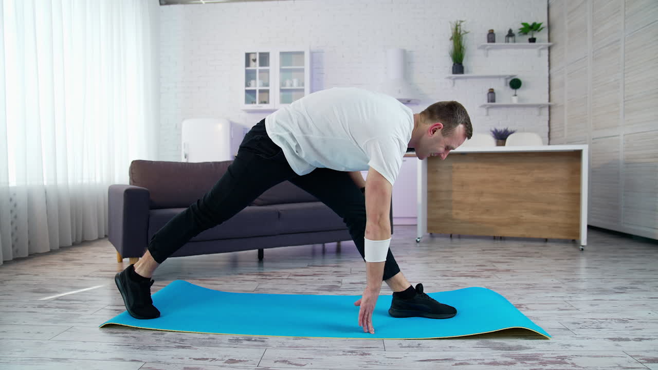 Young man doing fitness at home. Man in t-shirt and pants is doing exercises on mat at home in his spacious kitchen