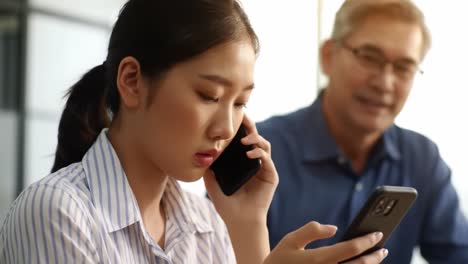 a woman is focused on her smartphone in a bright cafe, seemingly engaged in a conversation or browsing. a man is present in the background, adding to the lively atmosphere.