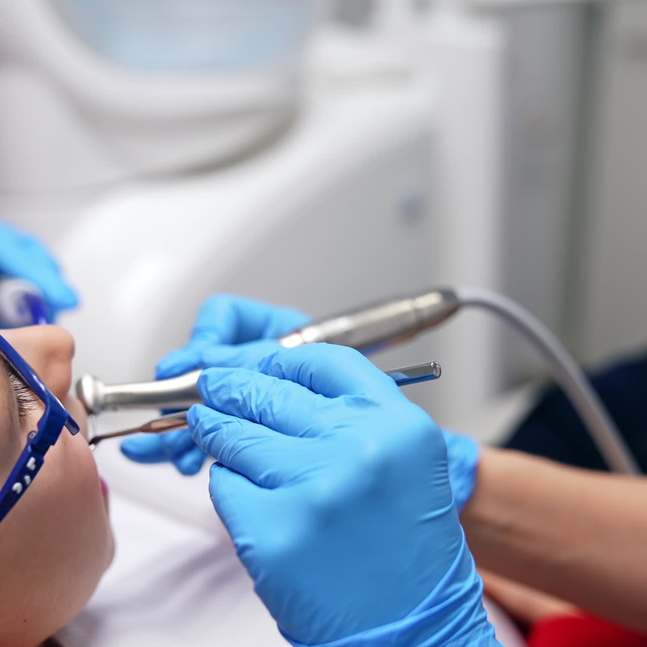 Hands in blue latex gloves take metal tool and drill machine to the boy's mouth. Teeth treatment in child dental cabinet. Close up. Blurred backdrop