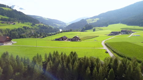 Chalets-En-Una-Llanura-Cubierta-De-Hierba-Cerca-Del-Lago-Braies-Pragser-Wildsee-En-Tirol-Del-Sur,-Italia,-Pedestal-De-Drone-Aéreo-Revela-Disparo