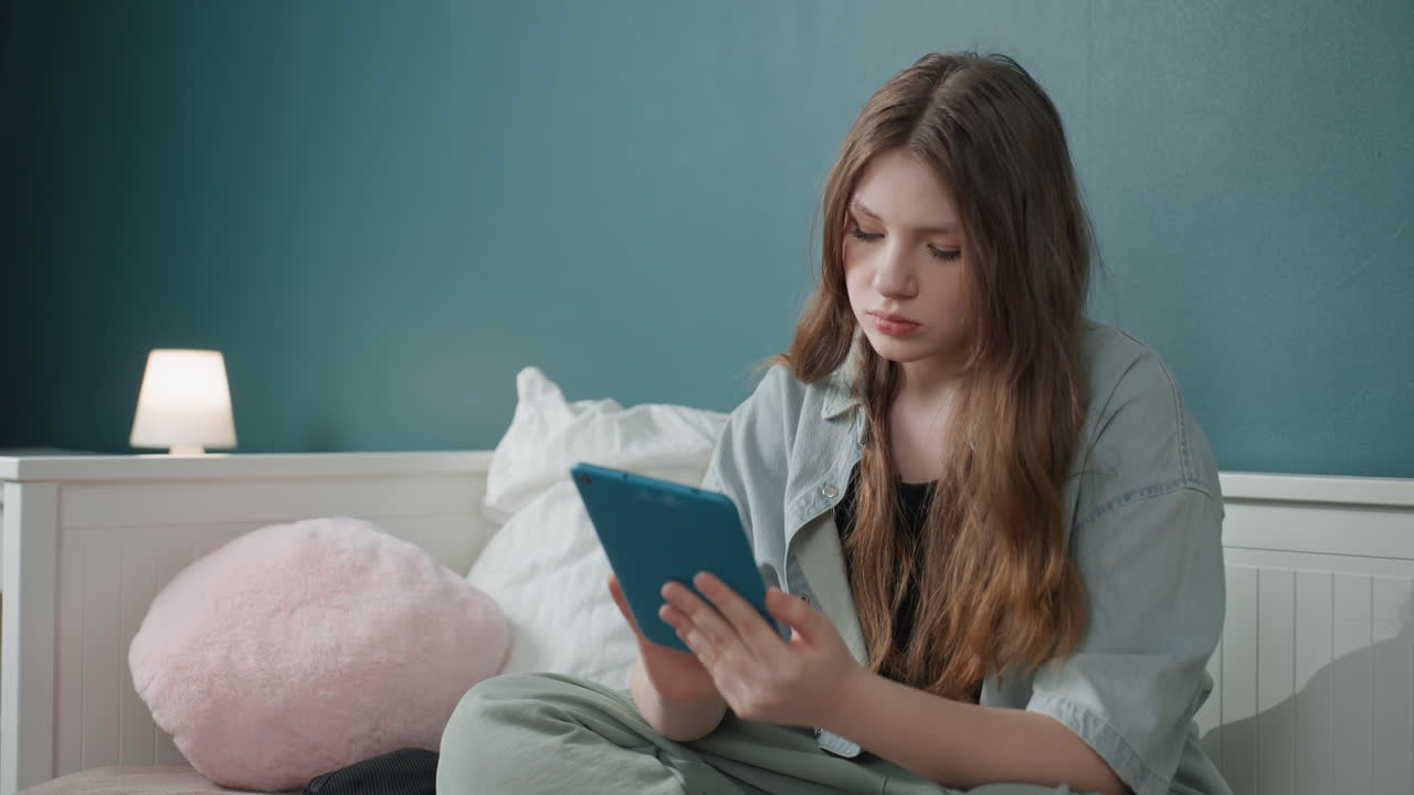 Young woman on bed reading book, soft lamp glow, teal wall, cozy pillows, attentive expression, slow page turning, focused study mood, introspective atmosphere, casual robe and relaxed posture