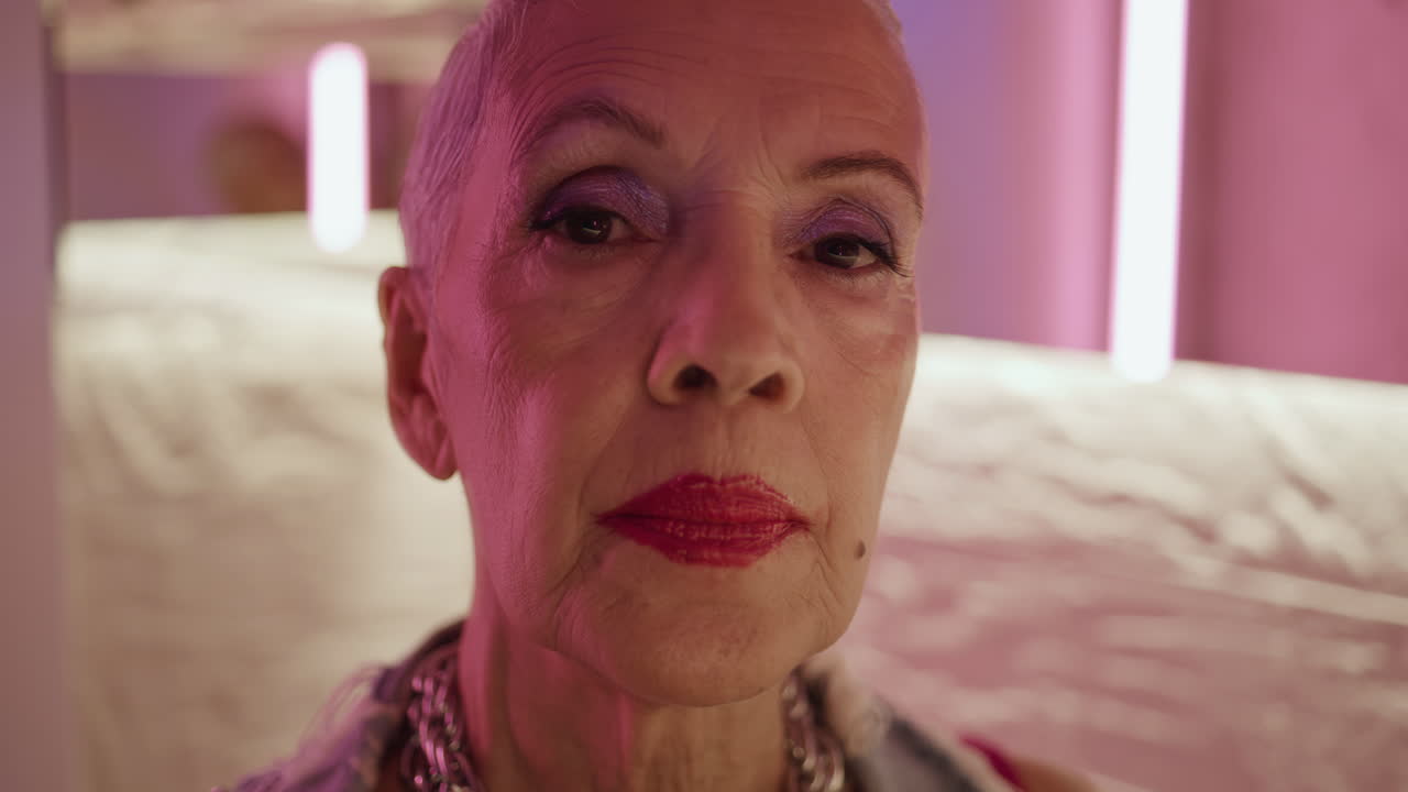 Portrait stylish pensioner looking camera in pink light. Serious cool woman