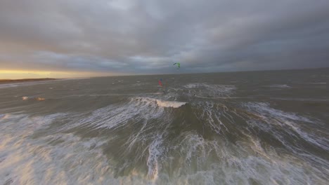 Luftaufnahme-Von-Zwei-Kitesurfern,-Die-Aneinander-Vorbeifahren,-Während-Einer-Von-Ihnen-Springt