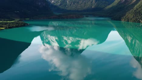 toma de un dron en movimiento de un lago natural verde transparente que refleja las montañas y las nubes