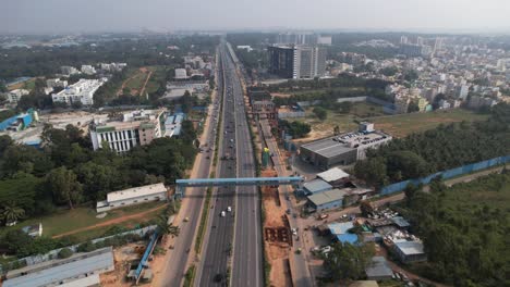 indian motorway in a cinematic aerial shot with metro train bridge construction visible above the service road and fast-moving automobiles