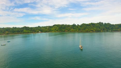 A-monohull-sailboat-anchored-in-a-calm-water-bay-near-the-shore-of-Costa-Rica-in-Drake-Bay-on-a-cloudy-blue-sky-day-in-paradise