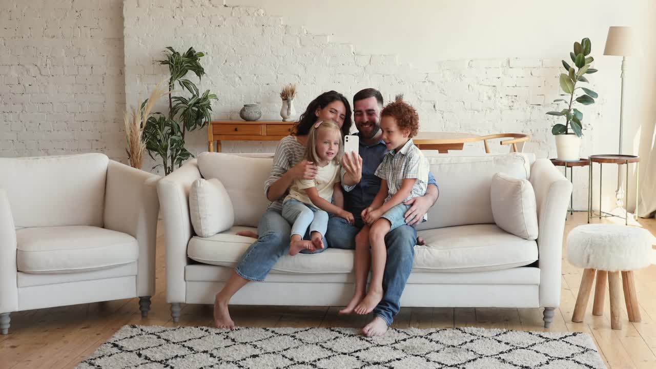 padres felices dos niños acurrucados en el sofá usando el teléfono