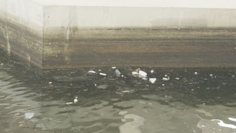 debris and floatsam of styrofoam cups and plastic float against concrete canal wall