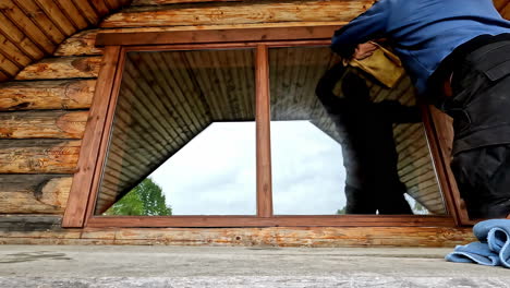 Timelapse of an adult man cleaning windows of a wooden house with cleaning cloth