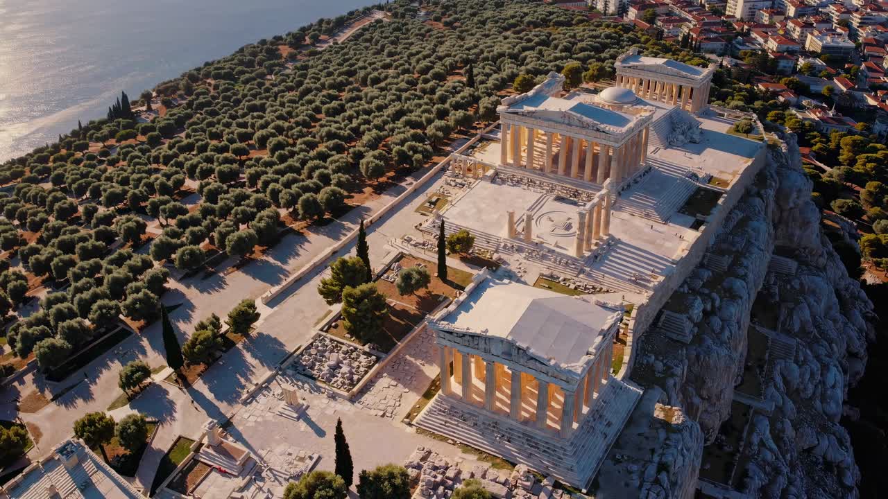 Aerial video capturing ancient ruins atop a hill, surrounded by olive trees and cityscape