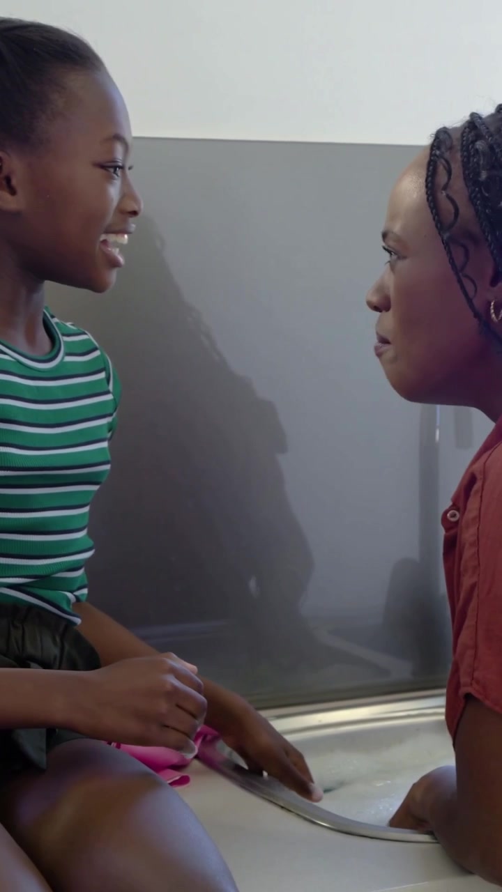 Vertical video: Smiling kid reaching sink at home counter, mom washing with pink gloves, copy space
