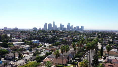 beautiful drone shot from a neighborhood of los angeles, california showing palm trees and the city skyline