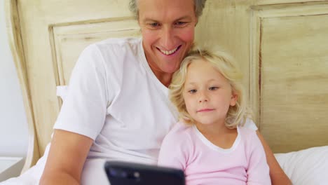Smiling-father-and-daughter-using-mobile-phone-on-bed-4k