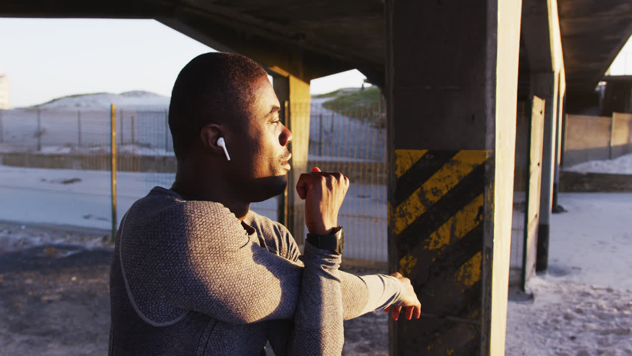 Fokuseret afroamerikansk mand, der strækker ud og motionerer udendørs ved solnedgang.