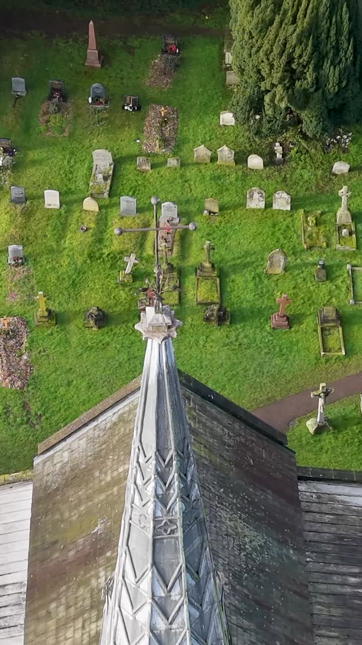 Chiesa di St Helens, Wheathampstead, campanile e croce sopra il cimitero e le tombe. Orbita fluida del drone in formato verticale attorno alla chiesa in pietra focaia e al campanile